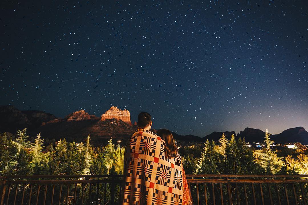 A couple, wrapped in a blanket, looks up at a starry night sky