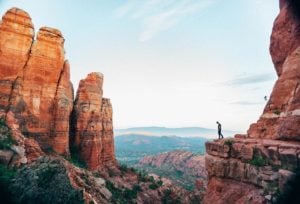 A person on the edge of a cliff look over the valley at more red cliff mesas