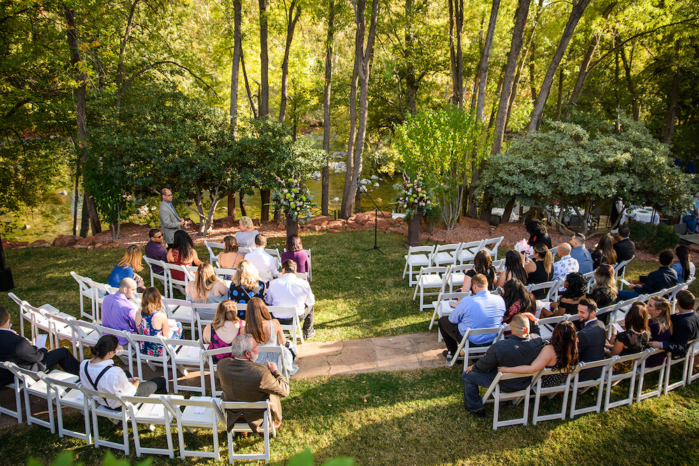 Outdoor fall wedding ceremony, the sun shines through the trees in the background.