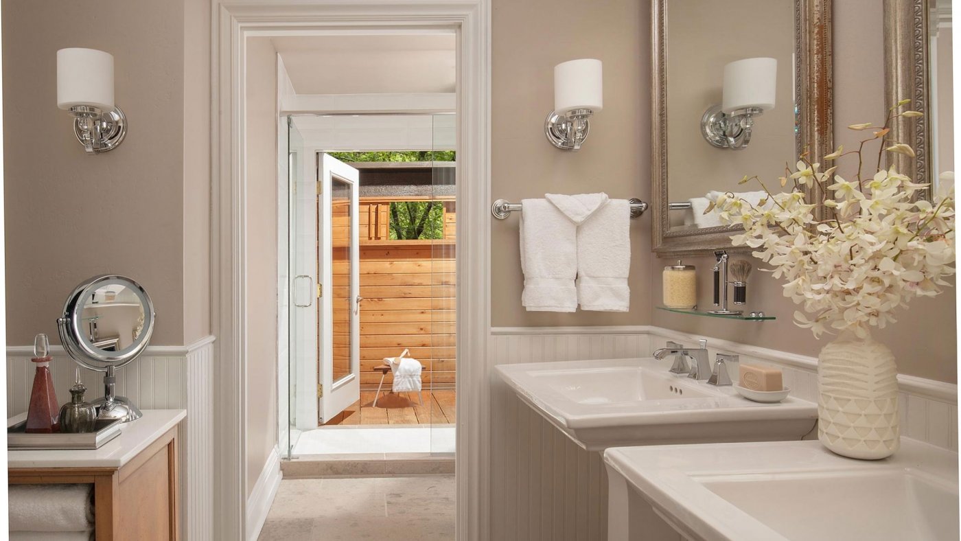 A two sink bathroom with a vase of white flowers.