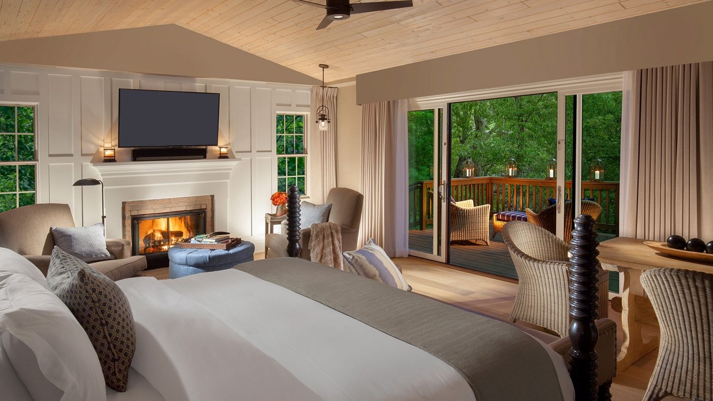 A bedroom with bed facing open balcony hanging over trees