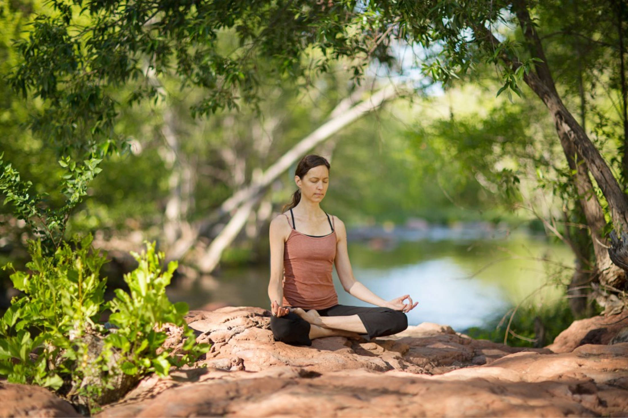 A woman meditating next to a river in the forest