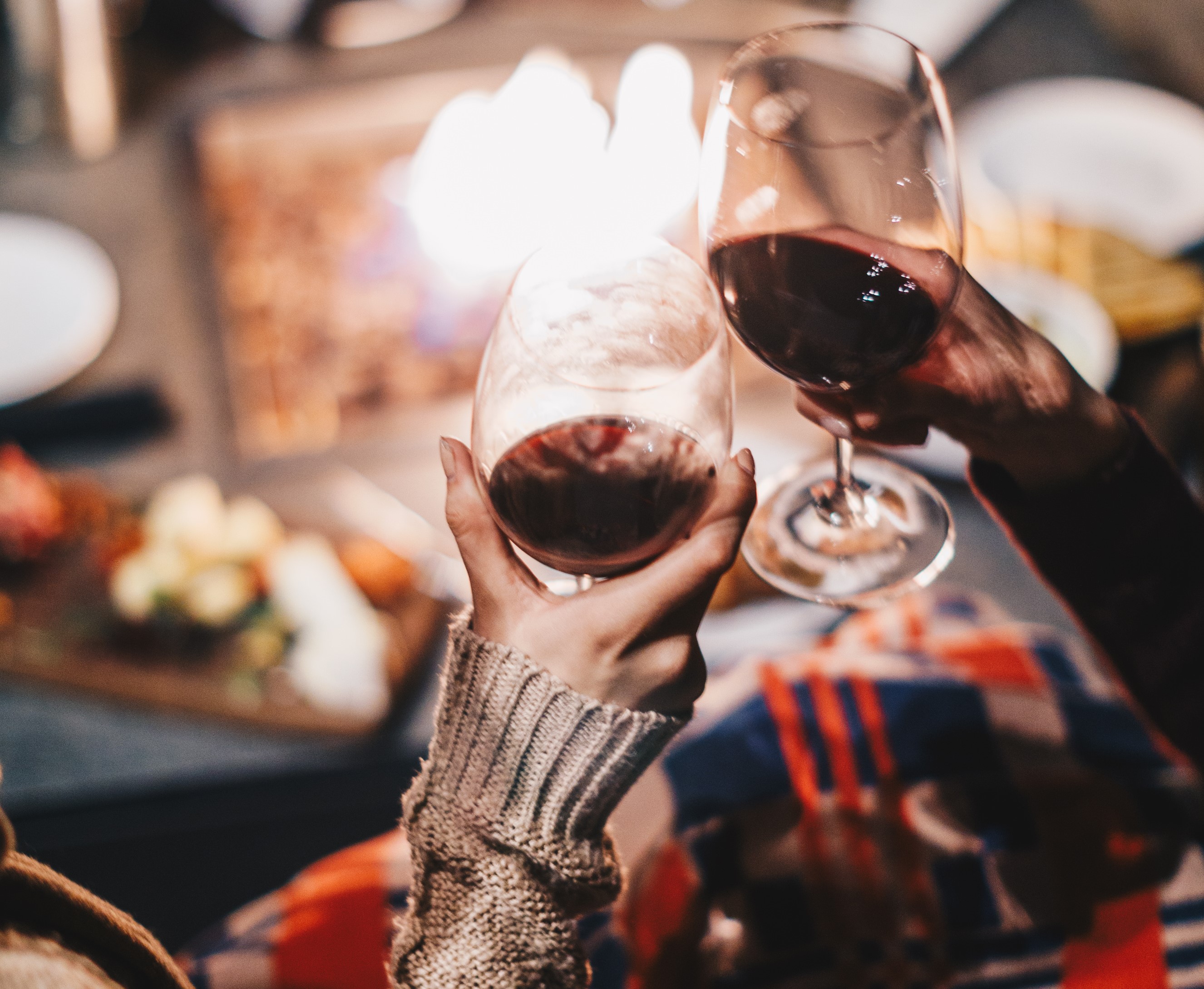 Close up of two hands clinking wine glasses over a cheese board and fire pit