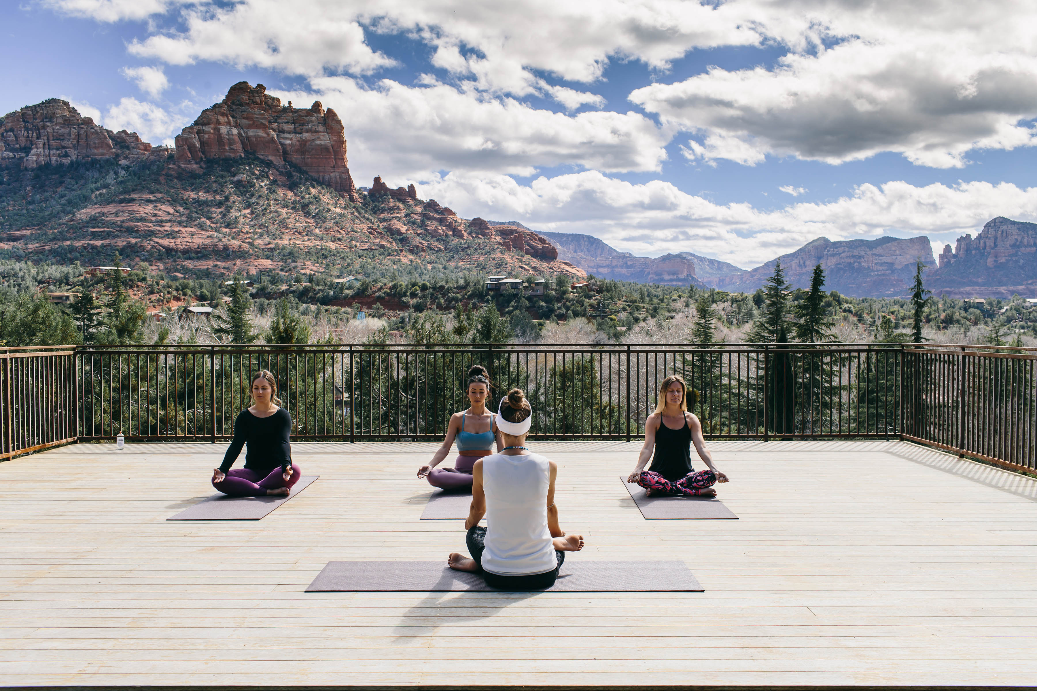 4 women practice yoga outside on a balcony overlooking the Sedona red rocks