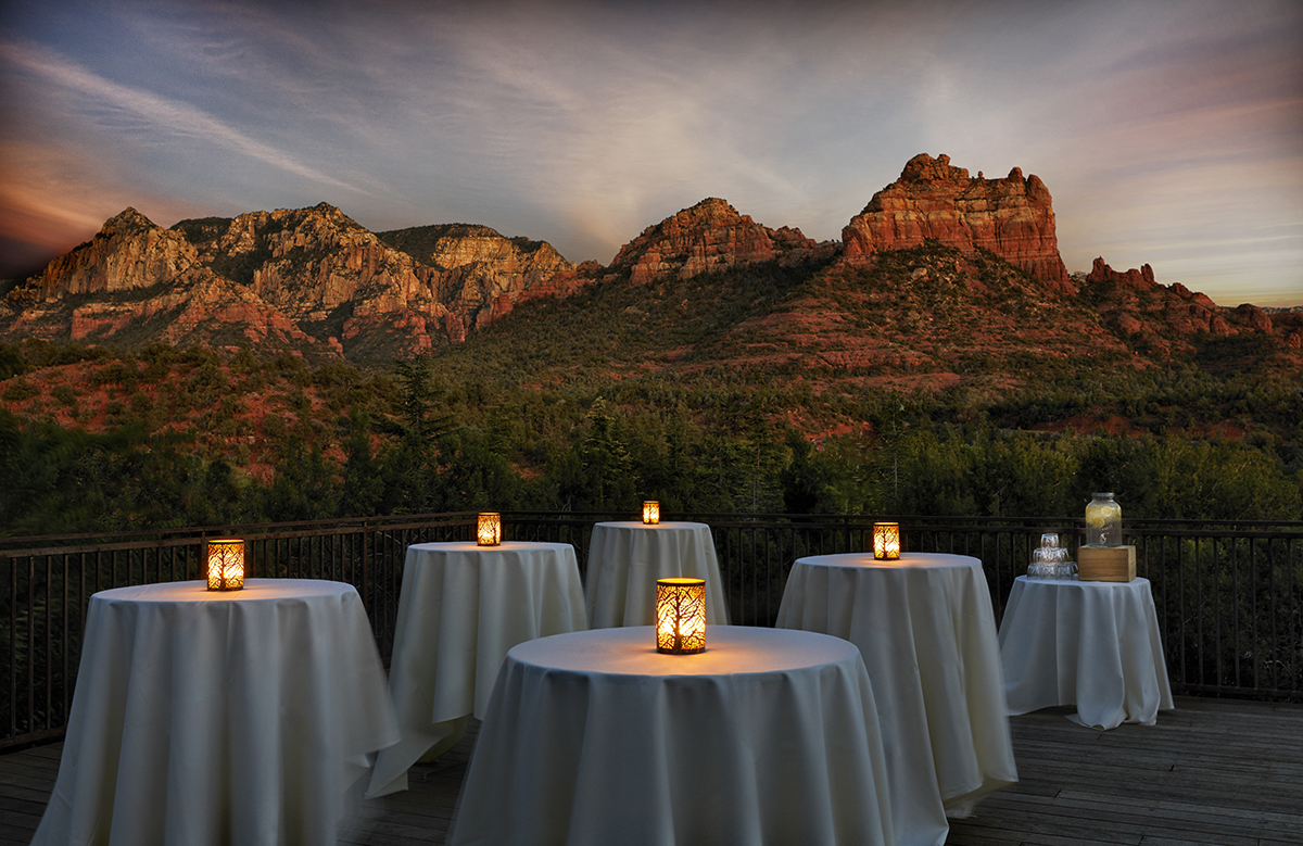 small tables with white linens and candles are set up outside overlooking the Sedona red rocks