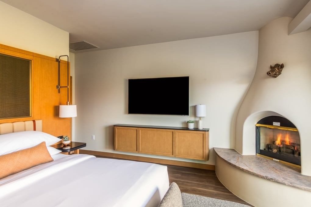 A hotel room with a bed, fireplace, TV, and wooden furniture.