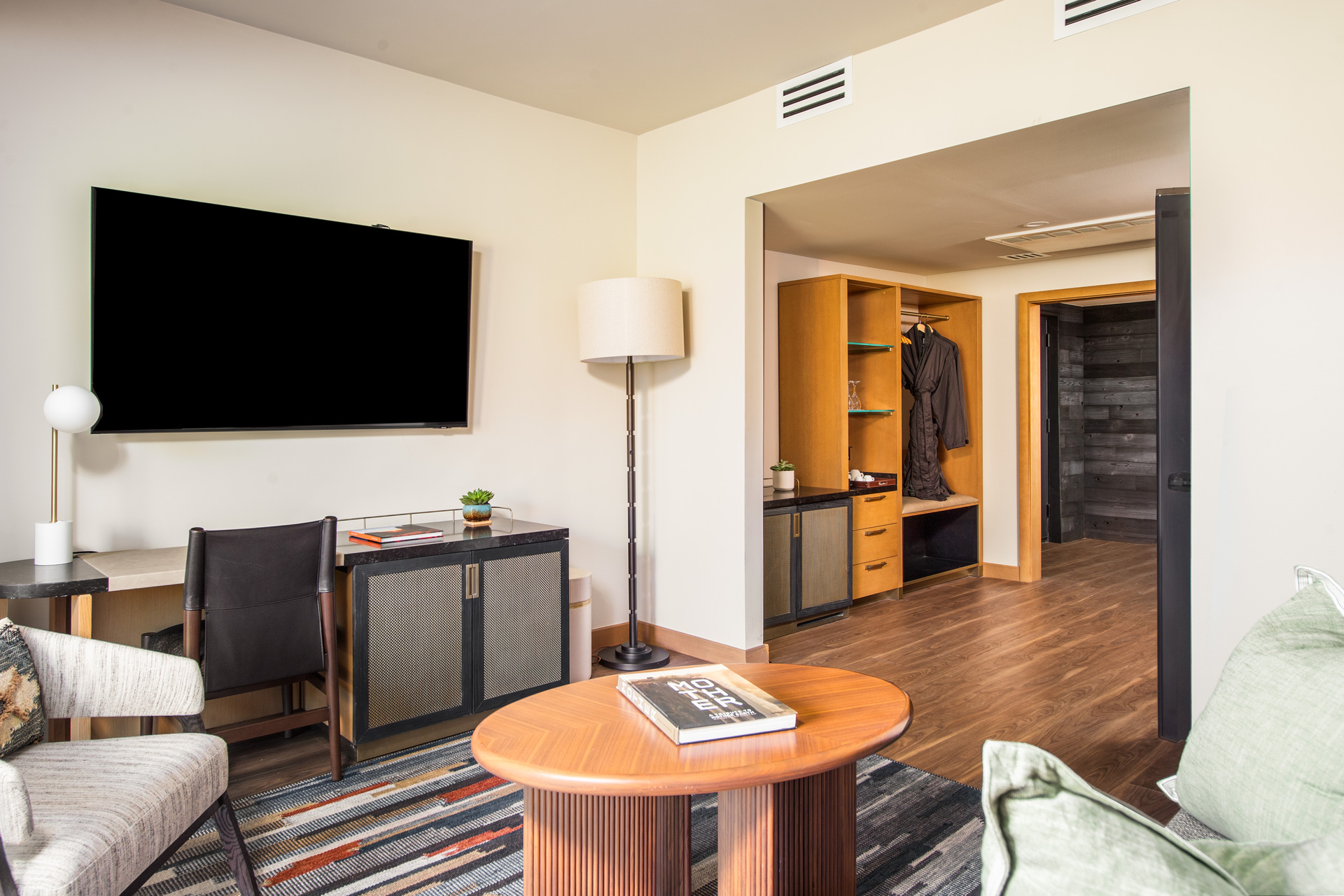 A hotel room living area with a TV, desk, chair, coffee table, and rug.