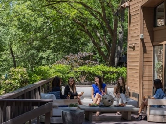 A group of women relaxing with drinks on a comfortable outdoor deck at the Creekhouse, shaded by large trees.