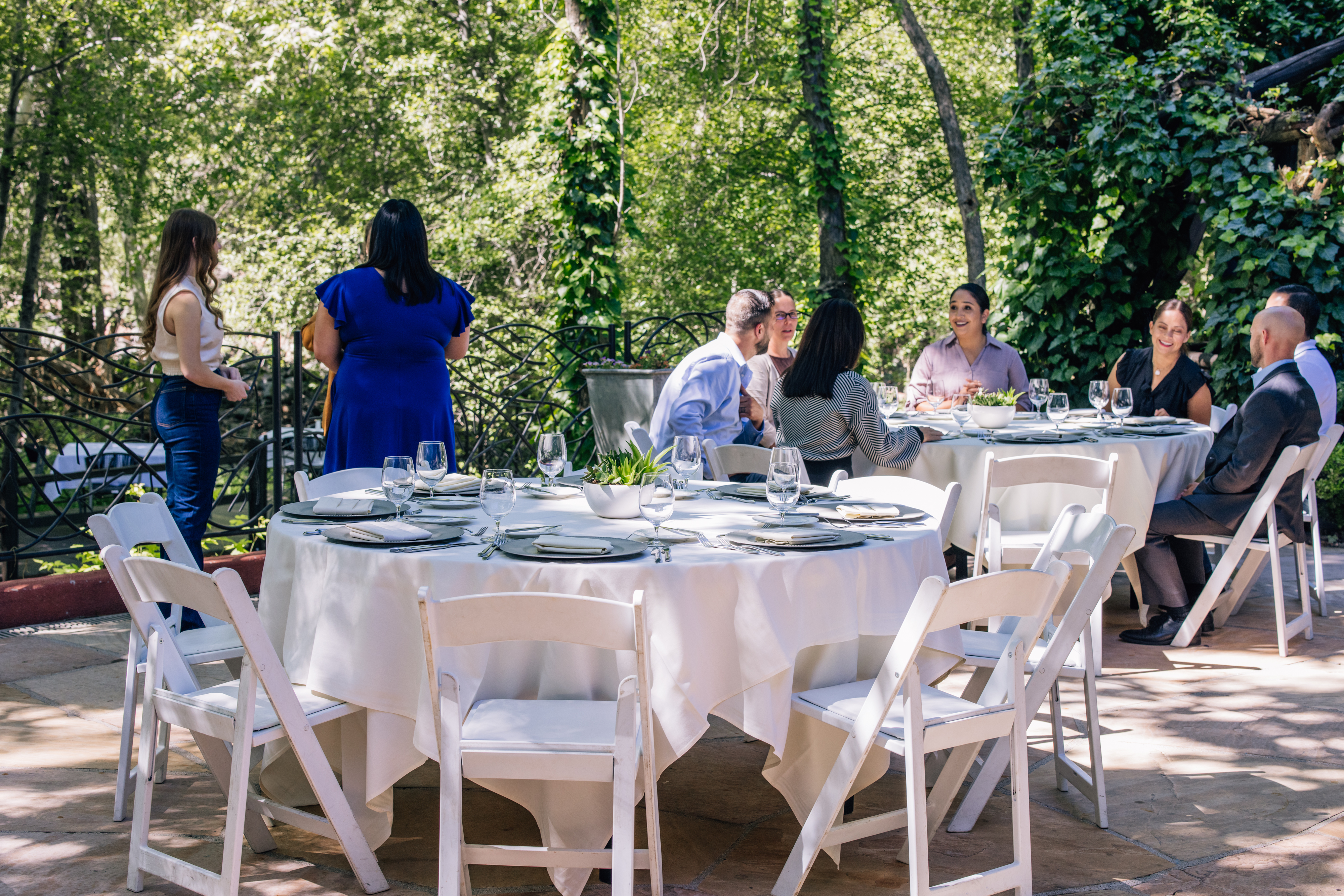 A group of people sitting at tables with white tablecloths and chairs in an outdoor setting.