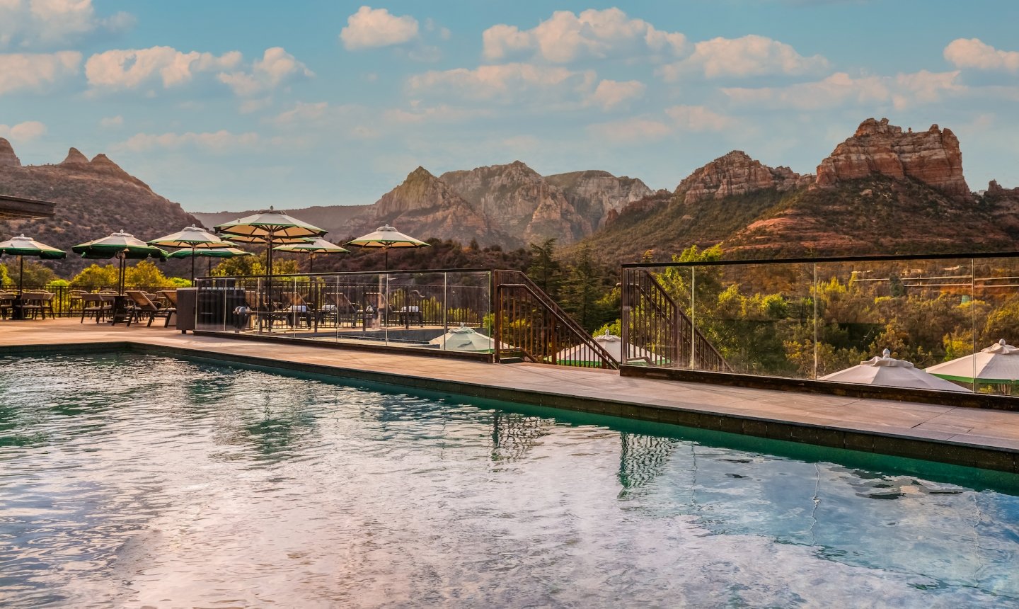 View from the edge of a resort pool, looking over the water at the deck, umbrellas, and a panorama of Sedona's red rocks.