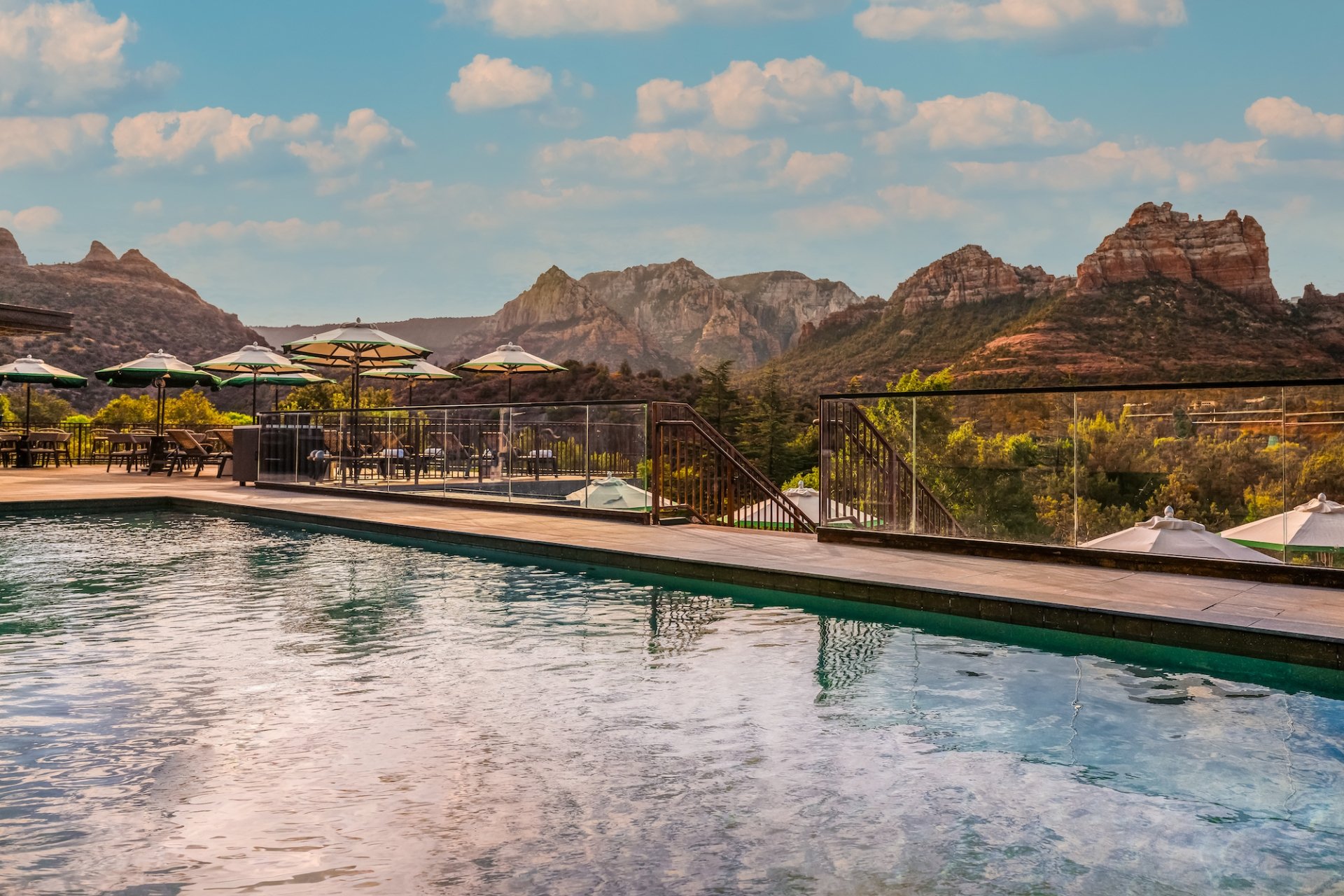 View from the edge of a resort pool, looking over the water at the deck, umbrellas, and a panorama of Sedona's red rocks.