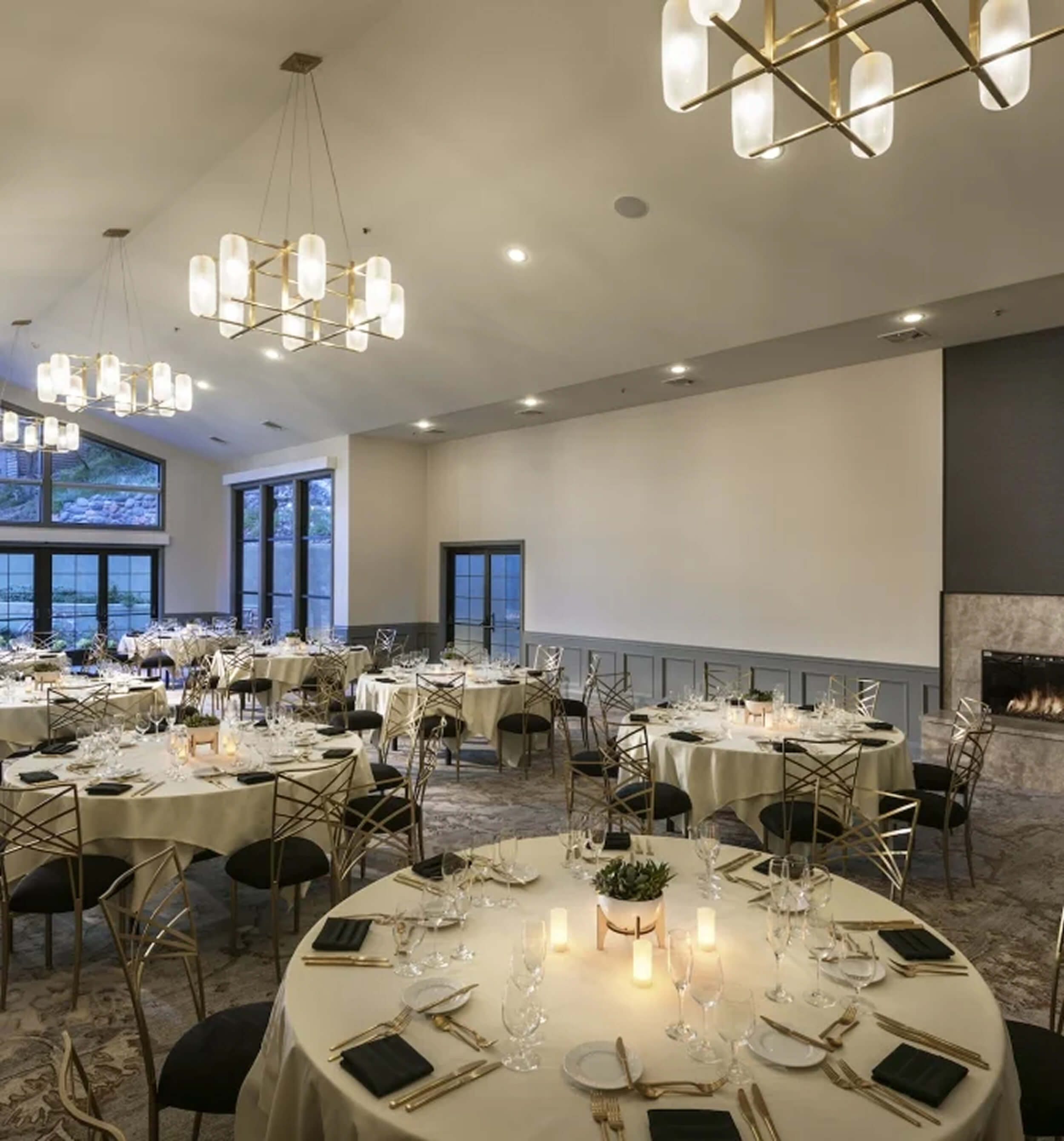 A large meeting room with round tables set for dining, a fireplace, and a chandelier.