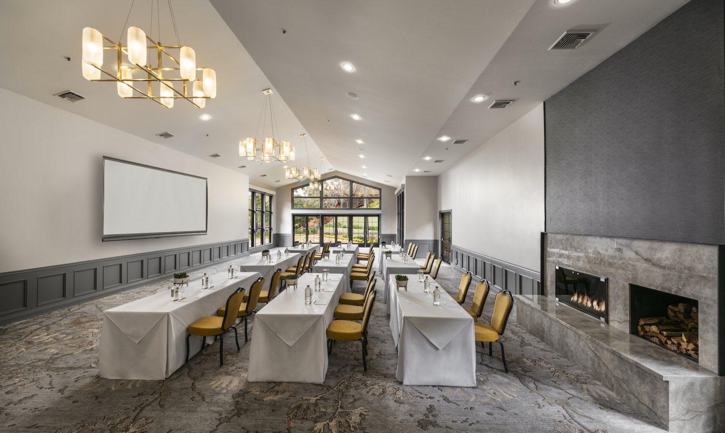 A modern ballroom in a classroom setup with long tables, a projection screen, and a large marble fireplace.