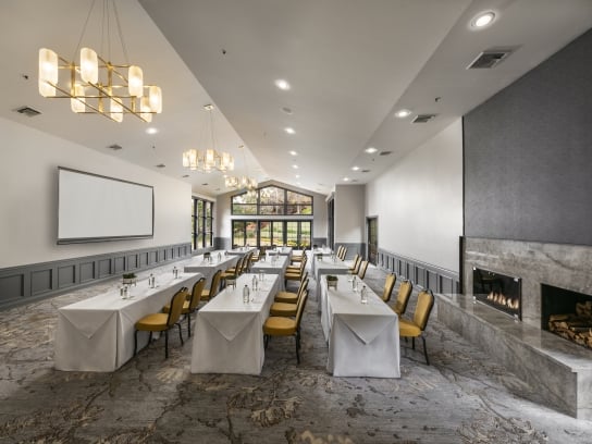 A modern ballroom in a classroom setup with long tables, a projection screen, and a large marble fireplace.