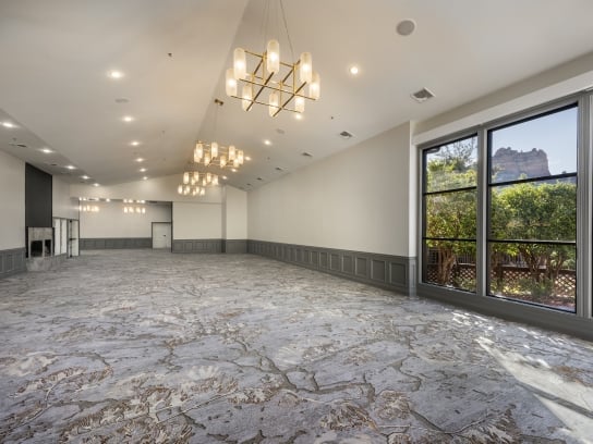 An empty, modern ballroom with patterned carpet, gold chandeliers, and a large window showing Sedona's red rocks.