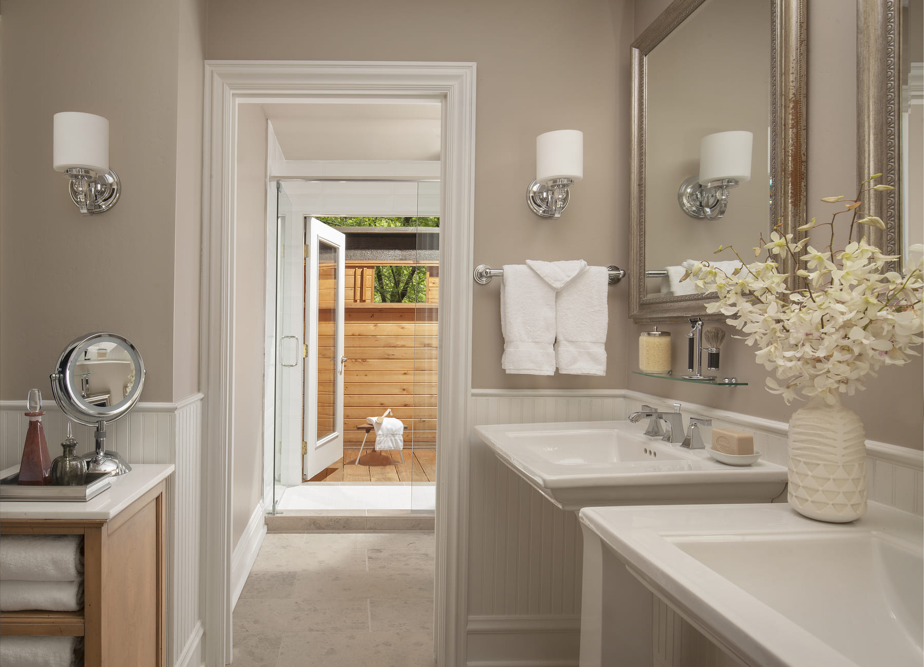 A clean and elegant bathroom with a double vanity, a shower, and a view of an outdoor area.