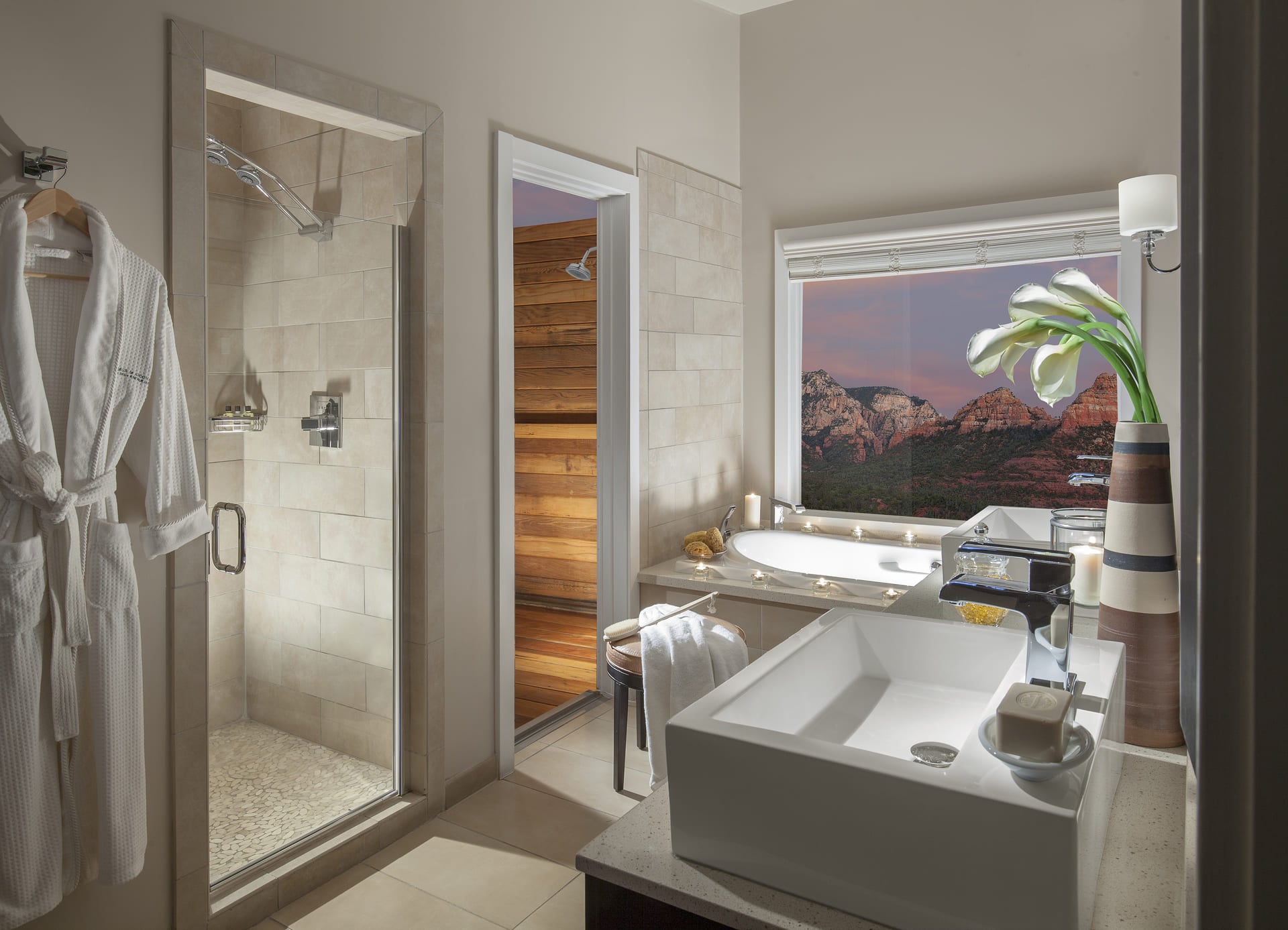 A bathroom with a shower, sink, and window showing a mountain view at sunset.
