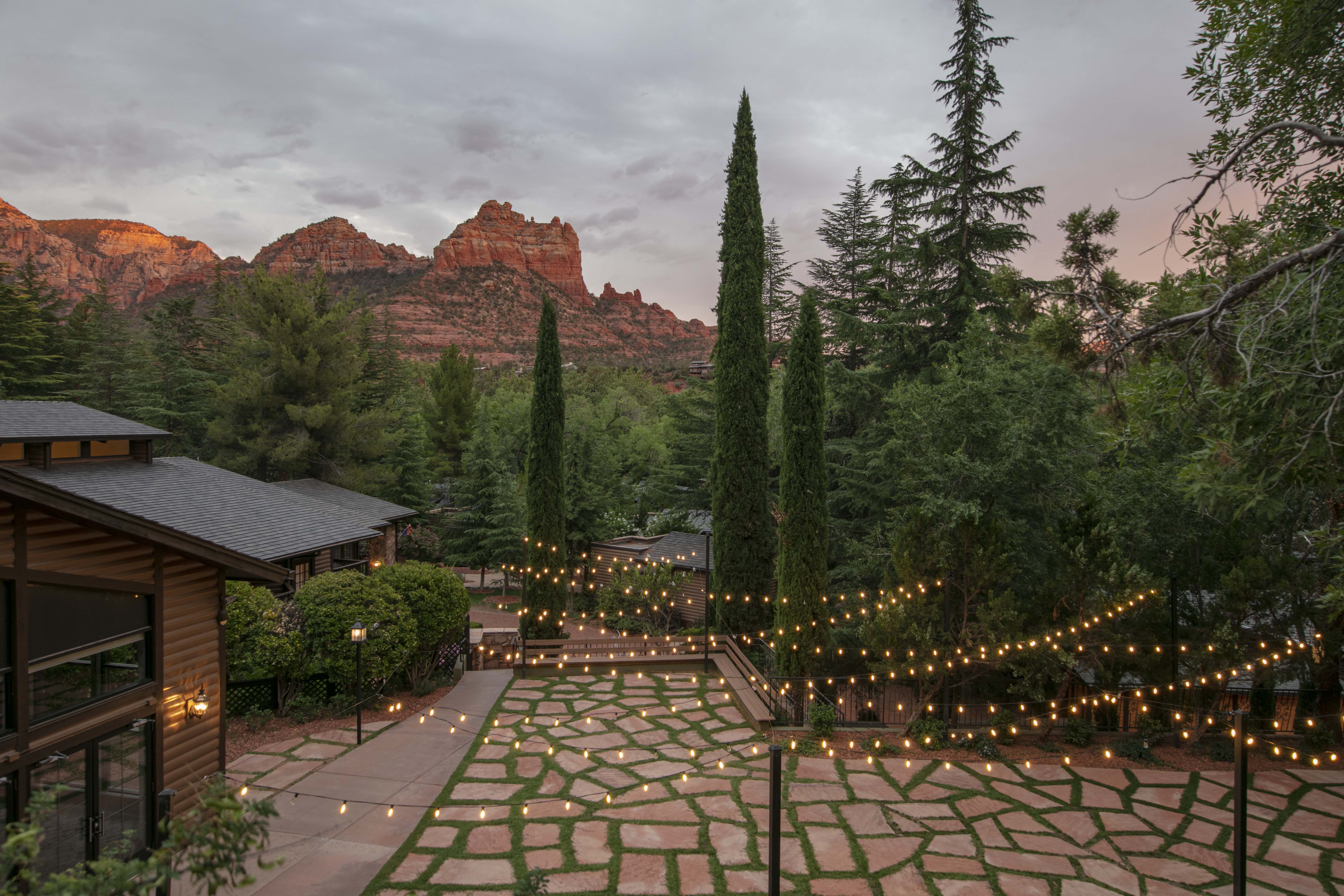 A decorated outdoor space with string lights, trees, and a view of red rock formations.