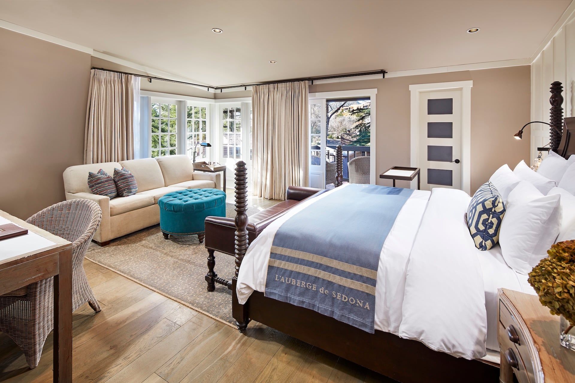 A wide-angle view of a hotel room with a king-sized bed, sofa, desk, and outdoor seating area.