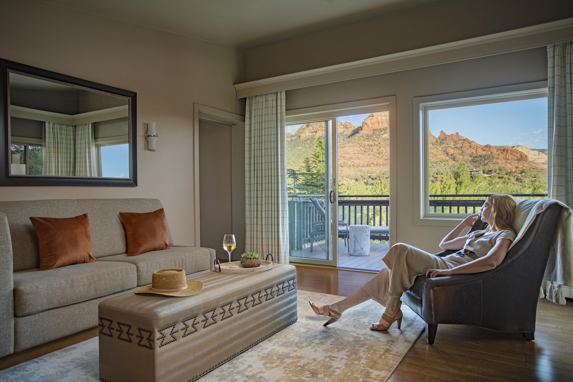 A living room with a sofa, armchair, and coffee table, looking out at a mountain view through a balcony door.