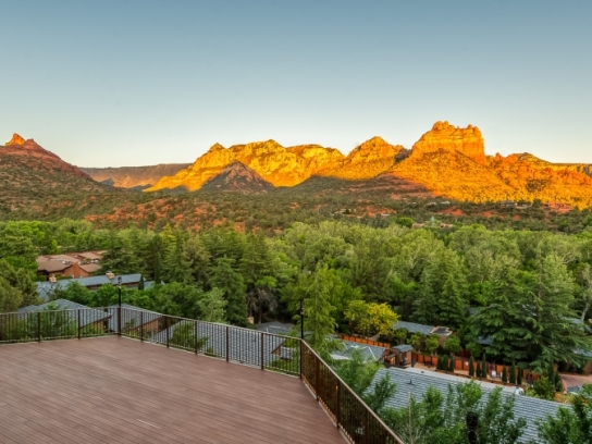 An empty wooden deck at sunset, offering a panoramic view of Sedona's red rock mountains glowing in the golden light.