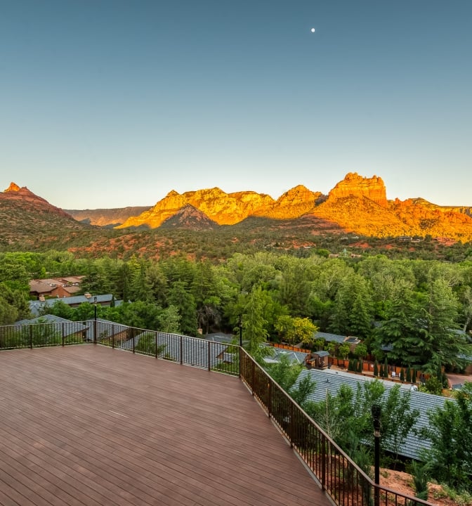 An empty wooden deck at sunset, offering a panoramic view of Sedona's red rock mountains glowing in the golden light.