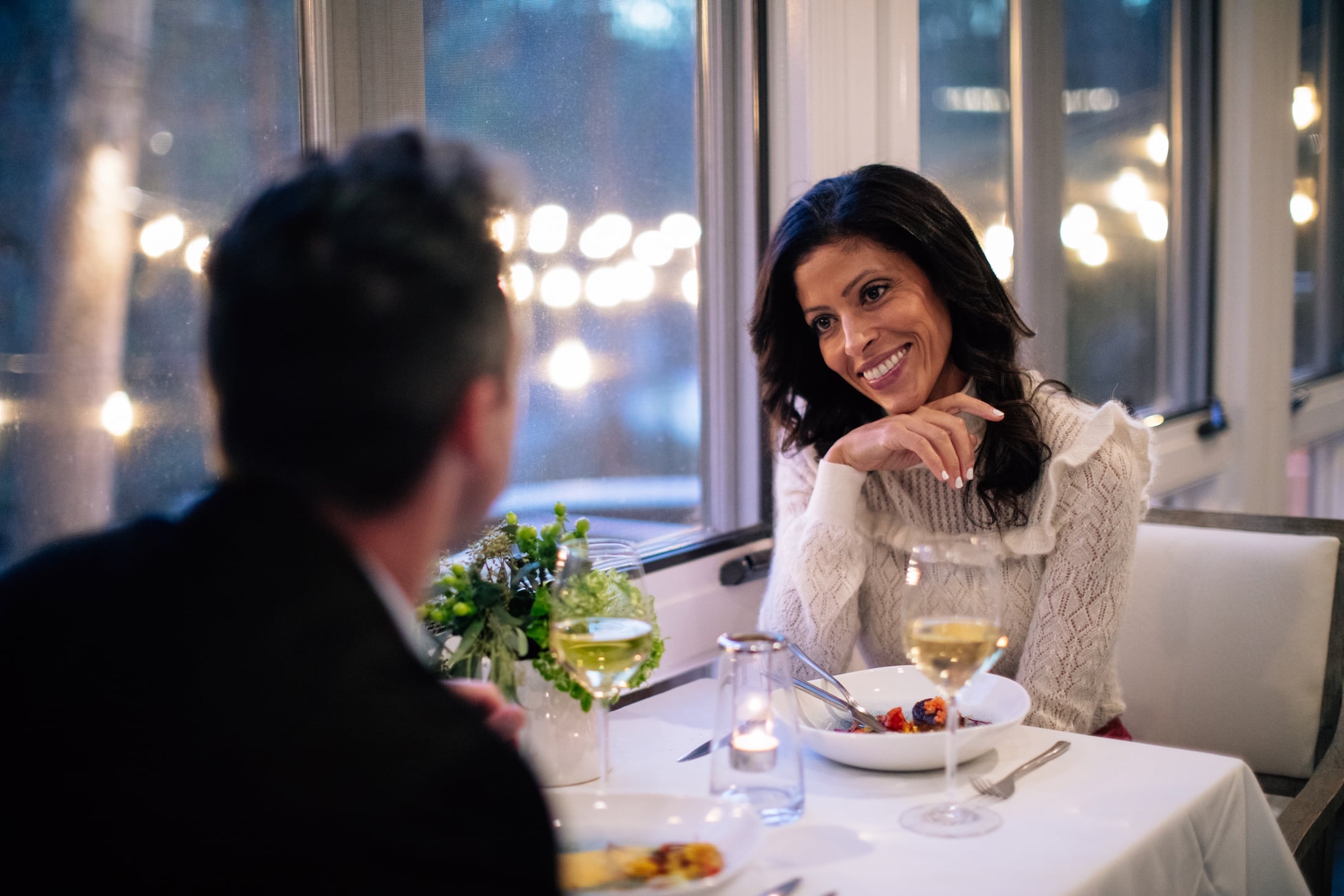 A man and woman sit at a dining table with wine and flowers.