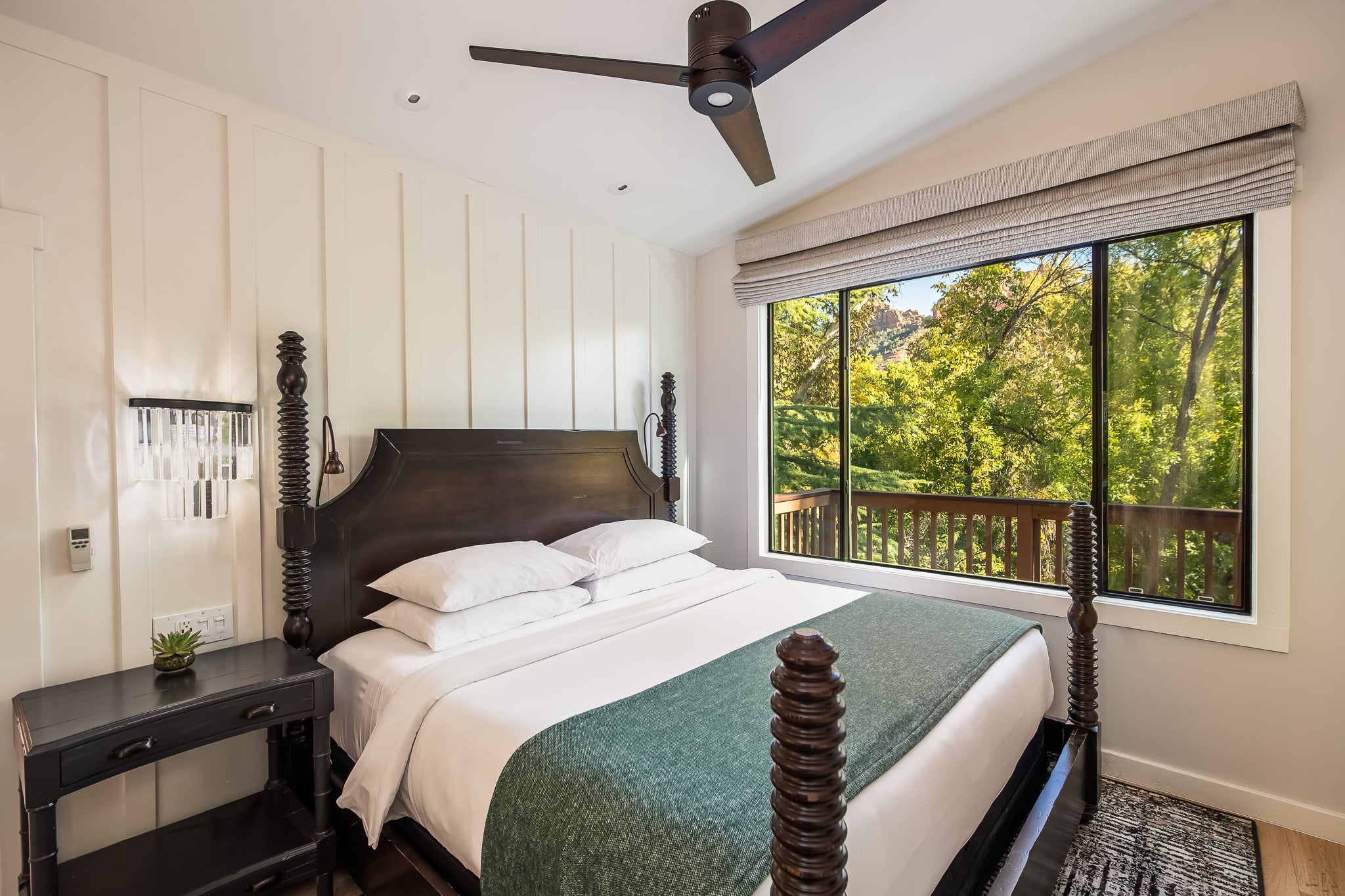 A hotel room with a large bed, a window overlooking trees, a ceiling fan, and a nightstand.