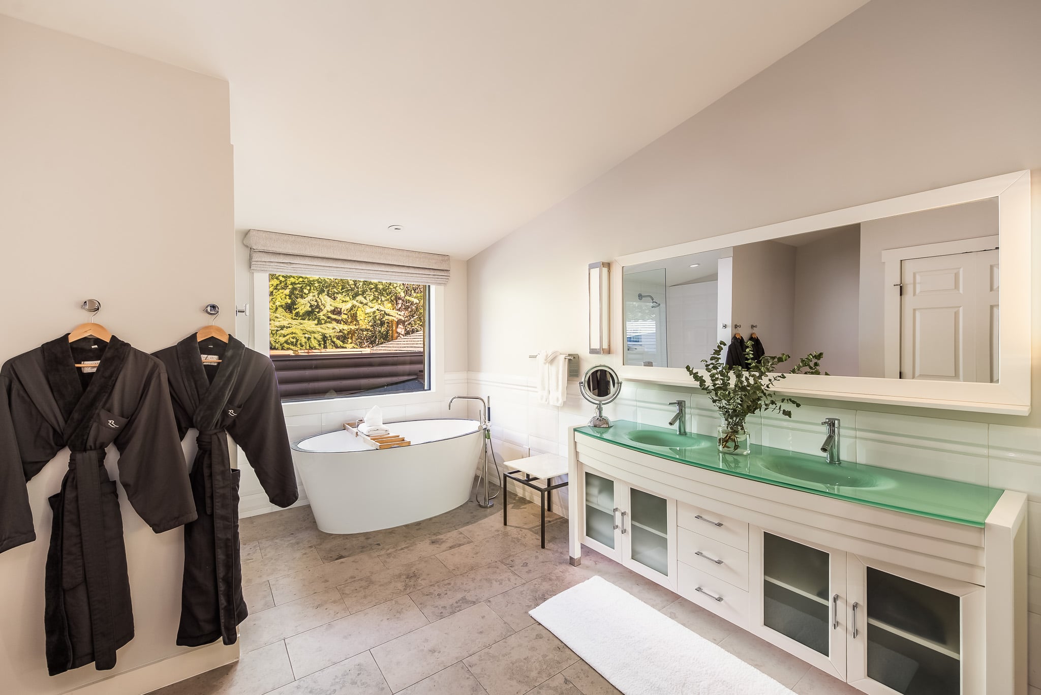 A clean and modern bathroom with a freestanding tub, double vanity, and robes.