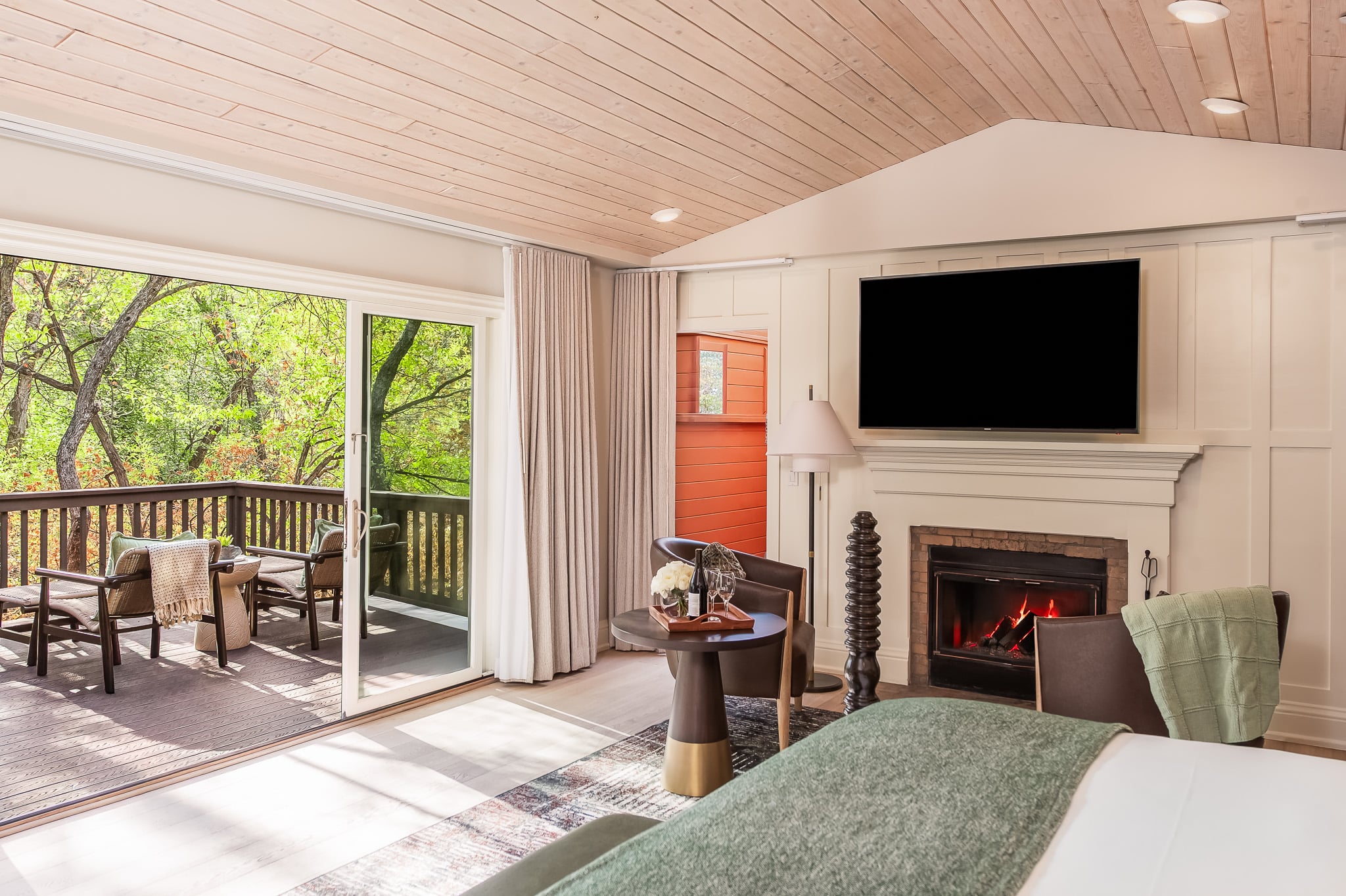 A wide-angle view of a hotel room with a fireplace, TV, balcony, and bed.