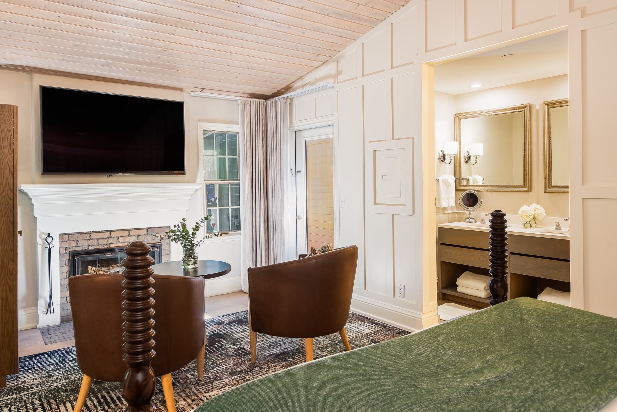 A wide view of a hotel suite with a fireplace, TV, dining table, bed, and bathroom.