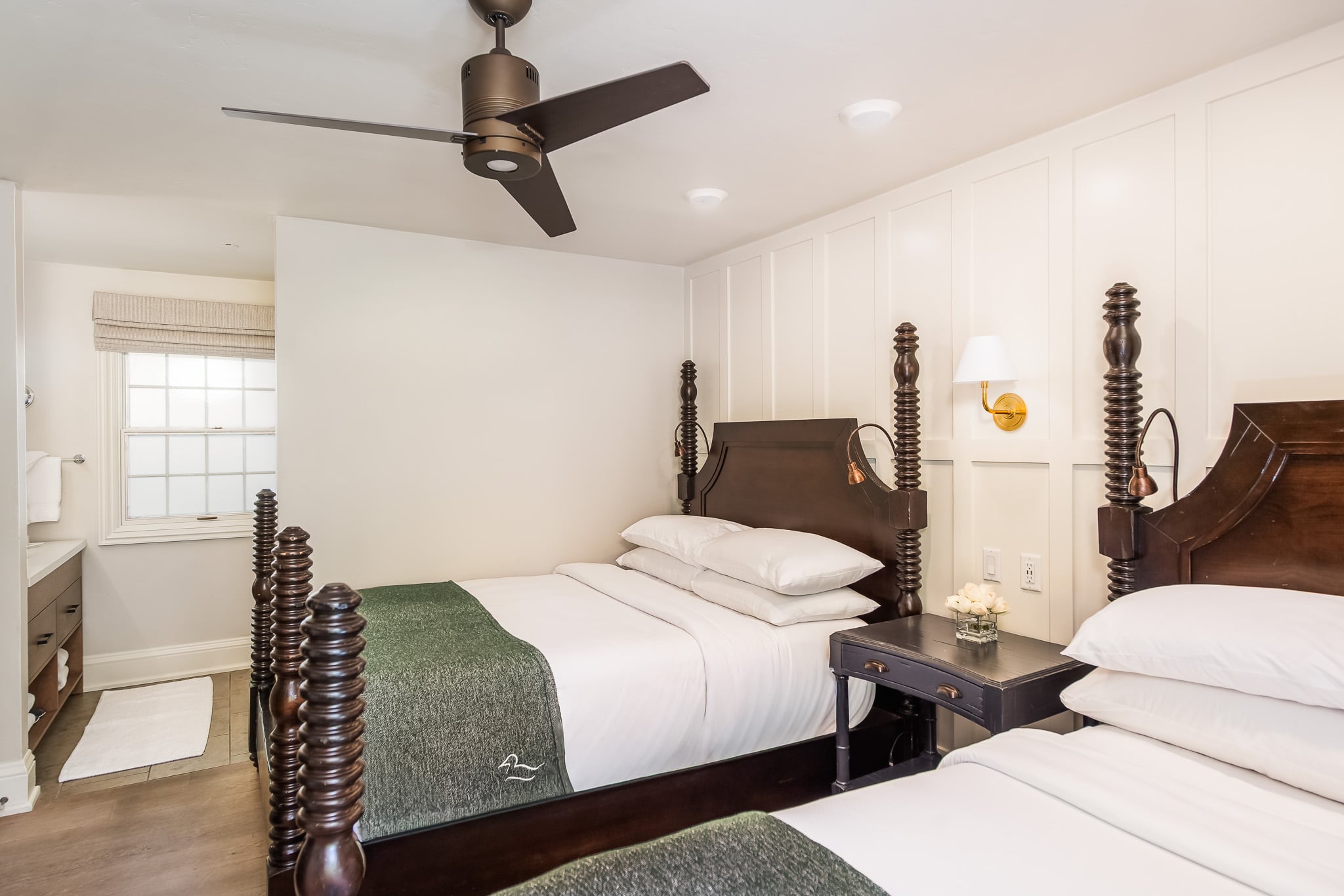 A hotel room with two twin beds, a nightstand, and a ceiling fan.