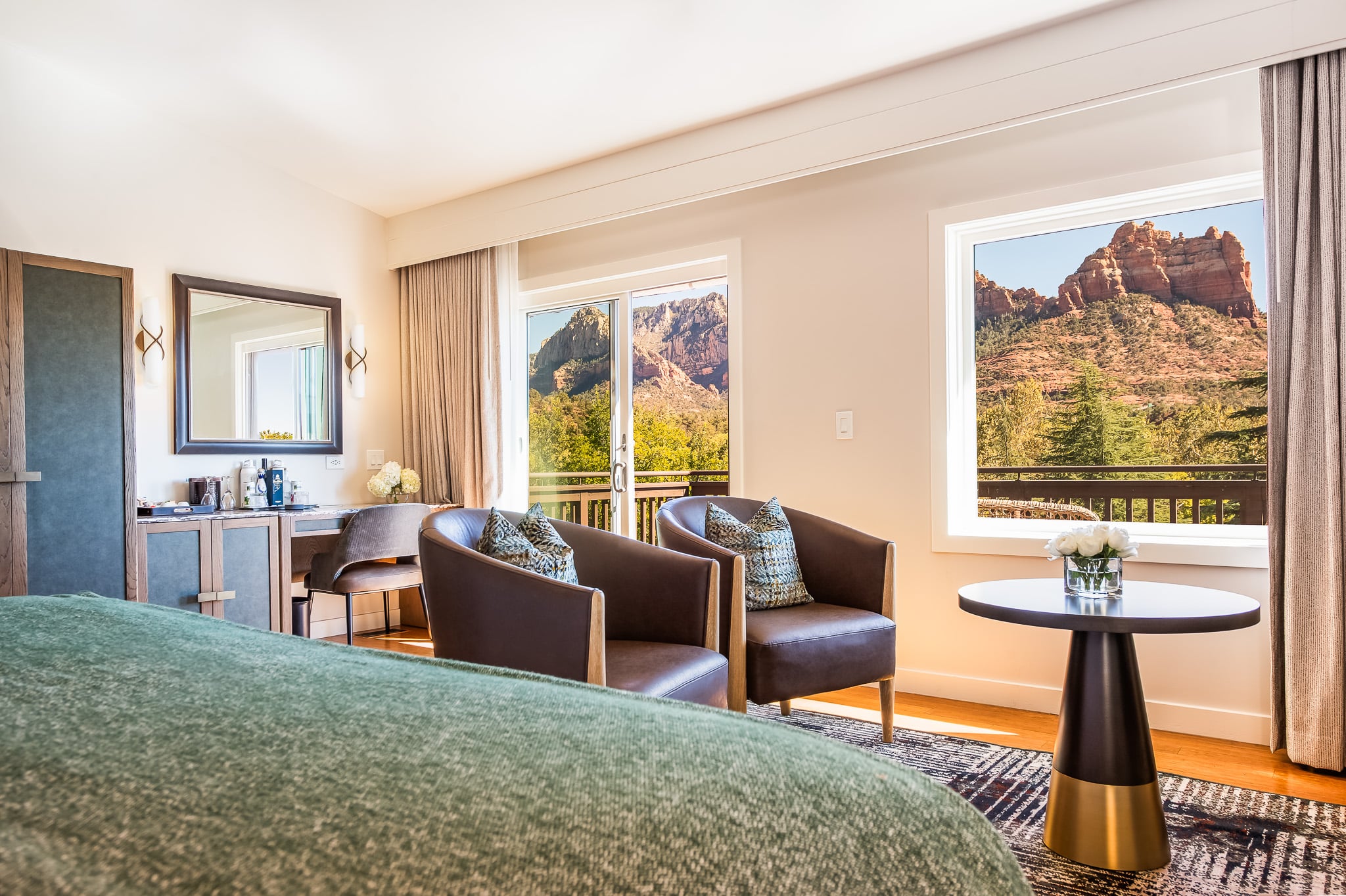 A hotel room with a bed, chairs, table, and a large window with a view of the mountains.