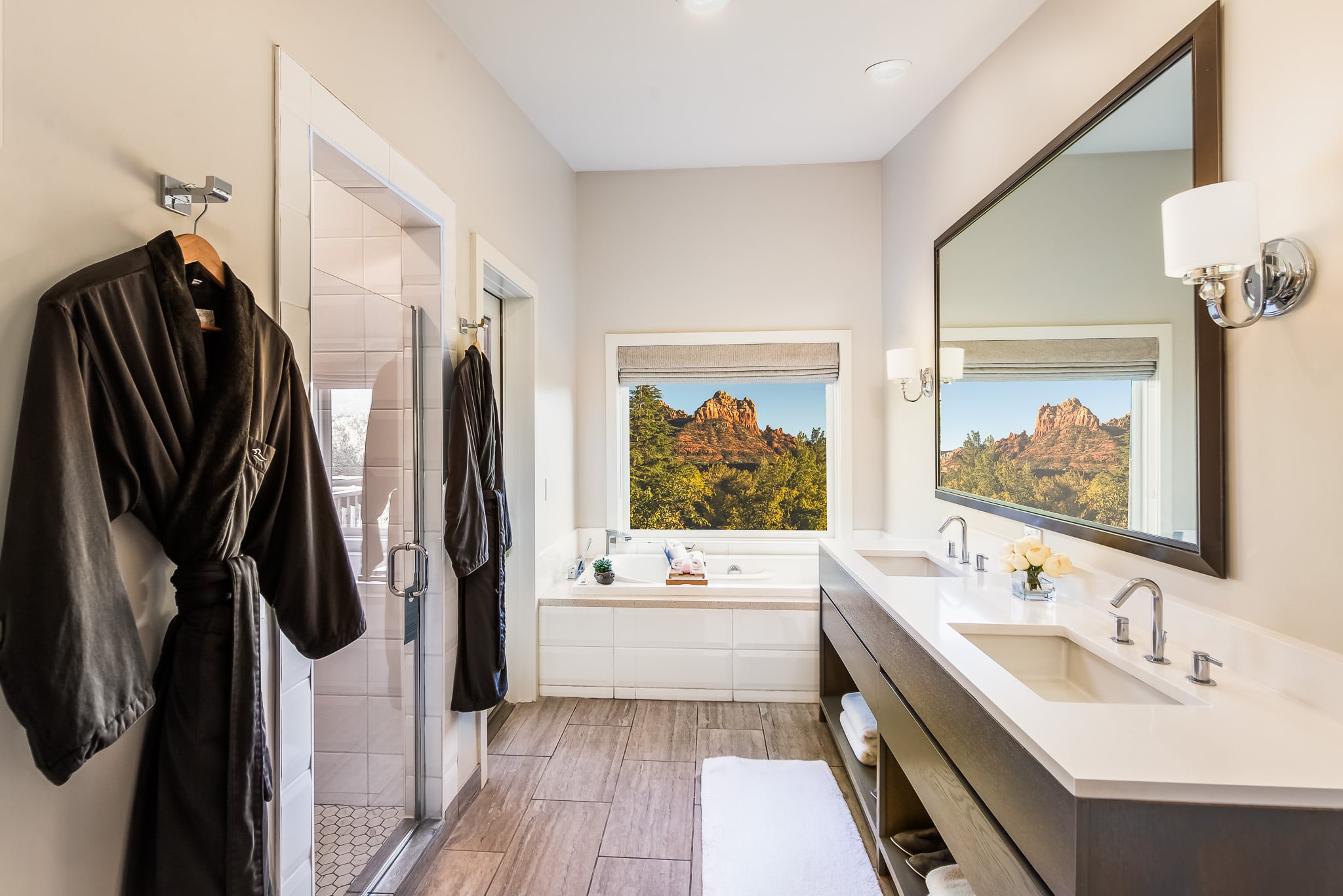 A modern bathroom with a double vanity, shower, bathtub, and window with a view