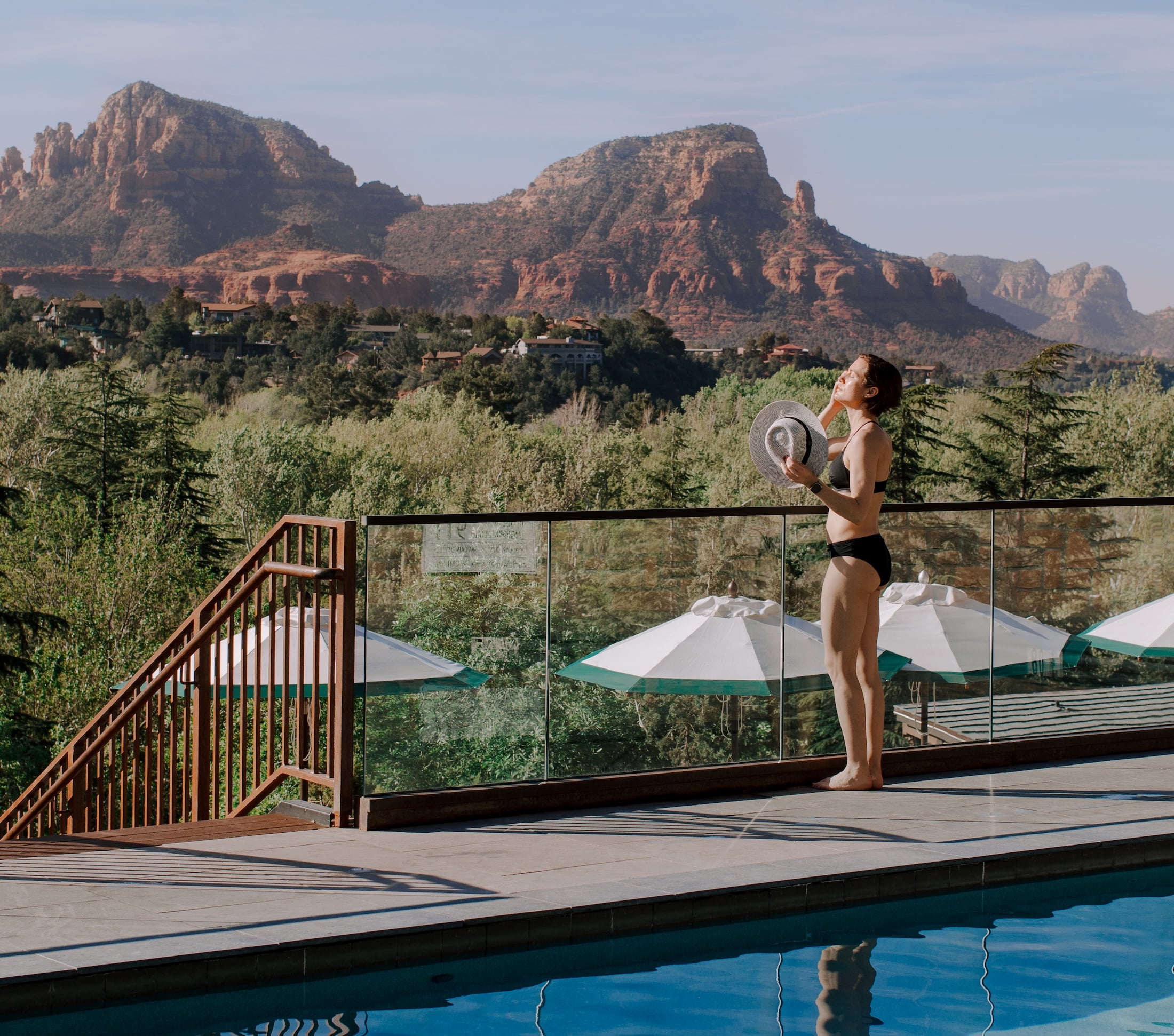 A woman in a black bikini stands by the pool with a volleyball, looking out at the mountain view.