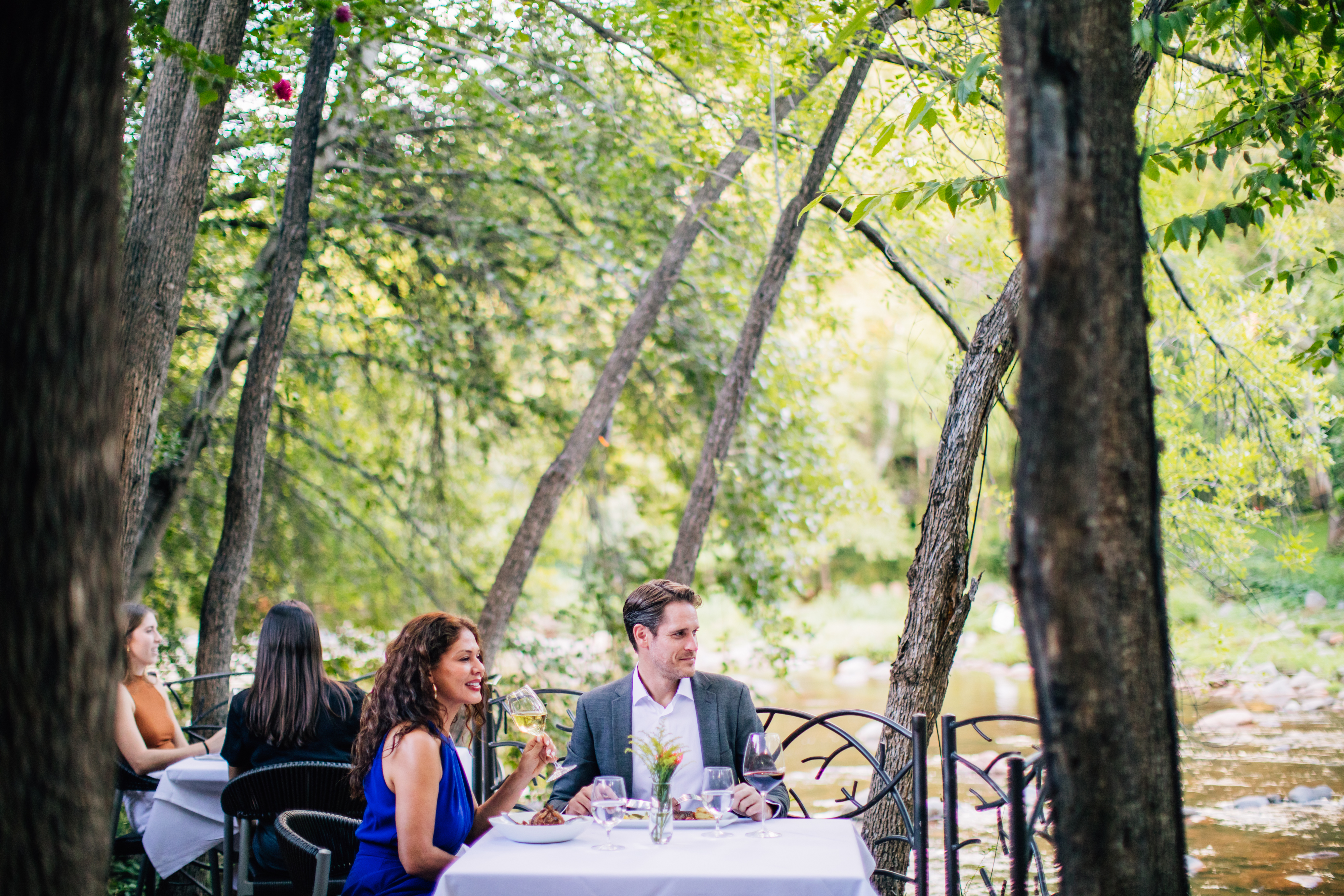 A couple is having a romantic dinner at an outdoor table surrounded by trees.